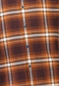 Camicia a quadri nei colori marrone scuro, arancione e bianco. Realizzata in tessuto intrecciato con una texture morbida, e bottoni neri lungo la parte anteriore.