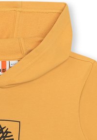 Sweatshirt à capuche jaune avec une texture douce, présentant un design graphique noir sur le devant et des coutures renforcées sur les bords.