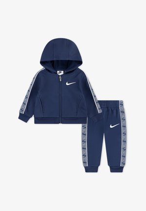 Conjunto de fato de treino azul marinho composto por um hoodie com fecho éclair e calças, cada um com o logo da Nike em branco. Listras em contraste nas mangas e pernas. Tecido suave.