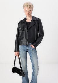 Jachetă de motociclist din imitație de piele neagră, cu fermoare și capse argintii, purtată peste un top negru, combinată cu blugi albaștri deschiși și o geantă patenta neagră.