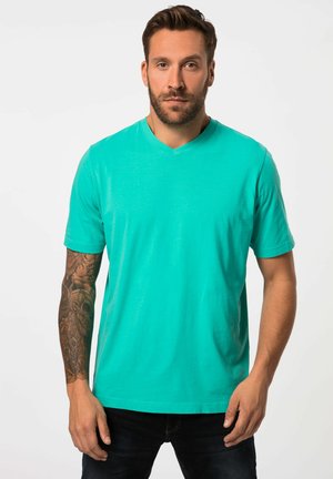 Camiseta de cuello en V color turquesa hecha de algodón suave. Mangas cortas, ajuste regular y textura lisa. Un par de jeans oscuros.