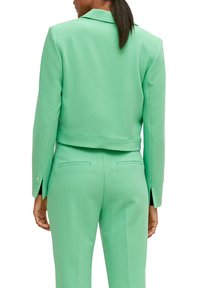 Miętowy zielony krótki blezer o fakturze jodełki, z wyciętym kołnierzem i mankietami na guziki, zestawiony z dopasowanymi, krójowymi spodniami z tylnymi kieszeniami.