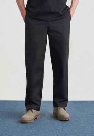 Czarne spodnie o prostych nogawkach, wykonane z gładkiej tkaniny, z prostym wzorem i bocznymi kieszeniami. Noszone z szarymi, zamszowymi botkami za kostkę.