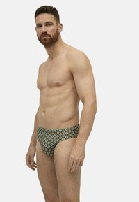 Bañadores de corte bajo en verde con un diseño geométrico en rojo y blanco, fabricados en un tejido texturizado. Ofrecen comodidad en su ajuste.