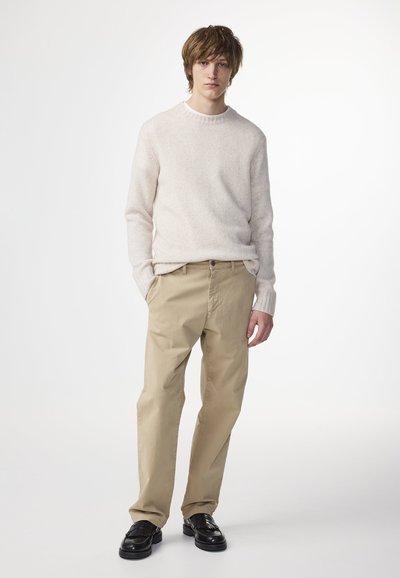 Maglione beige lavorato a maglia con colletto girocollo, abbinato a pantaloni leggeri color khaki. Mocassini neri completano il look. Design semplice e minimale.