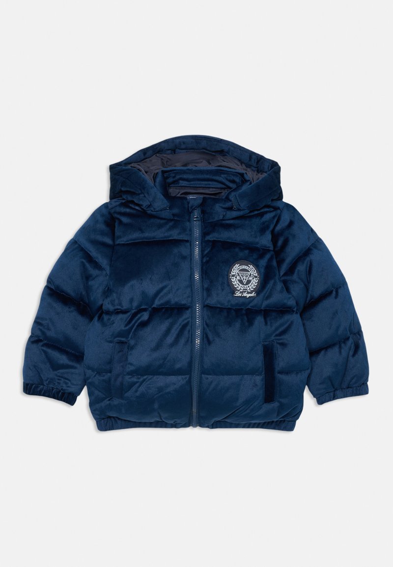 Tengerészkék pufi dzseki kapucnival, cipzáros záródással, elasztikus mandzsettákkal, és kerek logóval a mellkason. Puha, fényes textúra tűzött mintával.