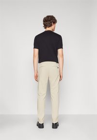 Svart kortermet skjorte kombinert med beige bukser. Buksene har to baklommer og er laget av et lett, glatt stoff.