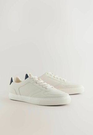 Weiße Leder-Sneaker mit strukturierter Oberfläche, dunkelblauem Akzent an der Ferse, runder Spitze und flacher Gummisohle.