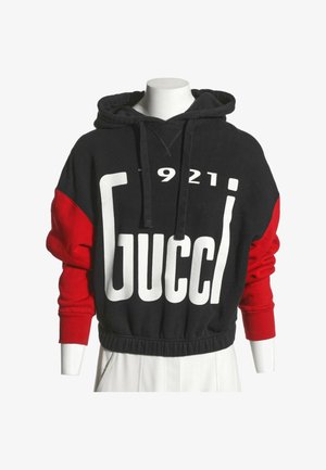 Sweat à capuche noir et rouge avec un grand texte blanc "Gucci" et les chiffres "1921" sur le devant, présenté sur un buste de mannequin blanc.