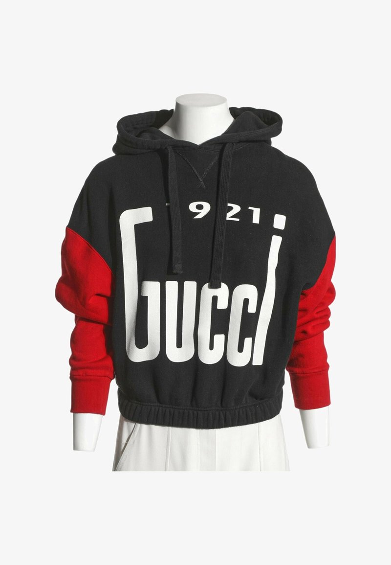 Sweat à capuche noir et rouge avec un grand texte blanc "Gucci" et les chiffres "1921" sur le devant, présenté sur un buste de mannequin blanc.