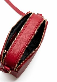 Rote Leder-Crossbody-Tasche mit zwei Reißverschlussfächern, strukturiertem Oberflächen und goldfarbenen Reißverschlüssen. Schwarze Innenauskleidung sichtbar.