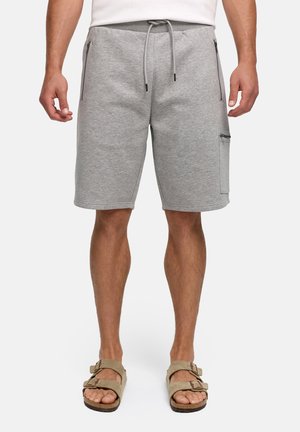 Uomo che indossa pantaloncini grigio chiaro fino al ginocchio con tasche frontali e laterali con zip, sandali beige a doppio cinturino, in piedi su sfondo bianco.