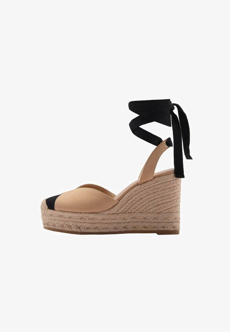 Espadrille compensée beige avec un bout en tissu noir, des brides en tissu qui se nouent à la cheville, et une plateforme en jute tressé. Présente une surface texturée.