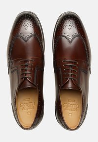 Scarpe brogue in pelle marrone con perforazioni decorative, punta rotonda e design con lacci. Presentano una texture liscia e una suola a contrasto.