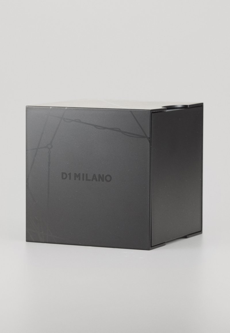 Schwarze rechteckige Box mit matter Oberfläche, die ein dezentes Designs Muster aufweist und auf einer Seite den Text "D1 MILANO" in Fettdruck zeigt.
