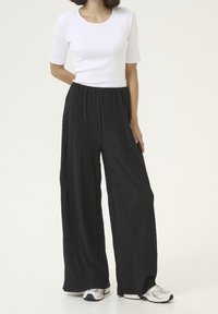 Black, wide-leg pants with a textured, pleated design, paired with a fitted white short-sleeve top. Features elastic waistband and sneakers.