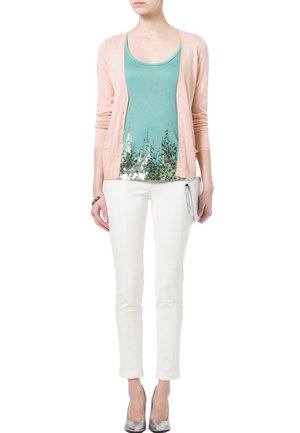 Heller rosa Cardigan über einem türkisfarbenen Tanktop mit Pailletten-Detail, kombiniert mit weißen Slim-Pants und silbernen Absätzen. Glattes Material und figurschmeichelnde Passform.