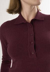 Bourgognefarvet langærmet sweater med krave, fem mørke knapper og blød strikket tekstur. Tætsiddende design fremhæver faconen.