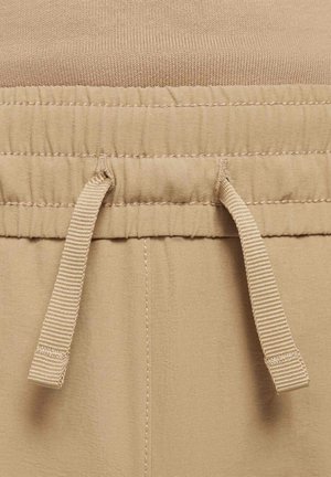 Nahaufnahme eines beigen elastischen Bundes mit einem gebundenen Stoffkordelzug an leichten Hosen oder Shorts.