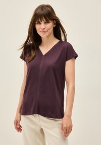 V-hals lila t-shirt med korte ærmer, strukturdetaljer ned ad midten, blødt stof og en afslappet pasform. Sammen med lyse bukser.