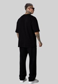 T-shirt en coton noir à coupe décontractée, associé à un pantalon noir assorti et des baskets blanches, vu de dos.