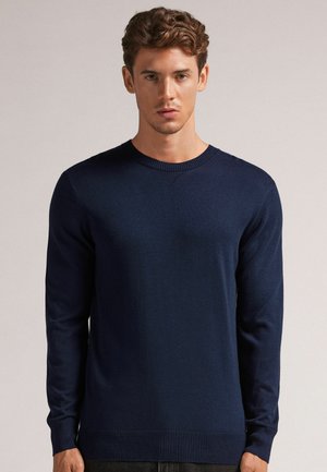 Pull en maille bleu marine avec des manches longues et un col rond. Présente des poignets et un ourlet côtelés, une texture lisse et aucune motif visible.