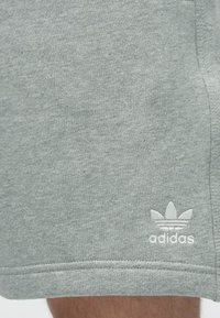 Γκρι βαμβακερά σορτς με απαλή υφή, ελαστική μέση και λευκό κεντητό λογότυπο Adidas κοντά στο τελείωμα.