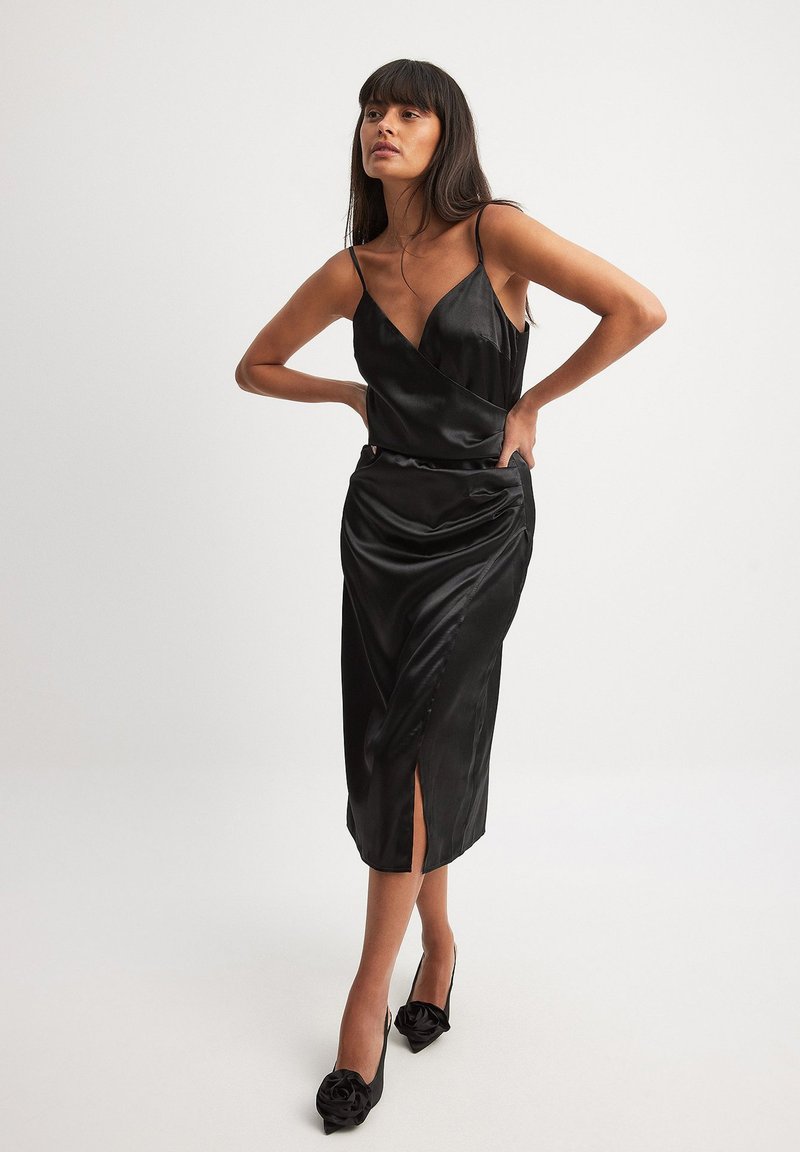 Juodas satino suknelė su giliu kaklu, reguliuojamais spageti petnešomis, iki kelių ilgio ir priekinėmis plyšiais. Dėvima su juodomis gėlėmis dekoruotomis aukštakulnėmis bateliais.