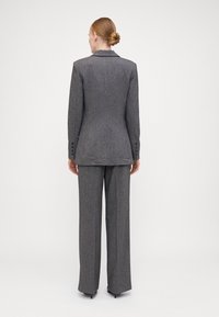 Completo in misto lana grigio con blazer sartoriale caratterizzato da rever a punta e dettagli con bottoni, abbinato a pantaloni larghi. Texture liscia.
