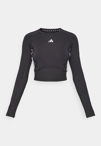 Črni dolg rokav, kratki top iz raztegljivega materiala, z belimi detajli in logotipom Adidas na prsih. Ozek kroj in rebrasta tekstura.
