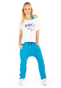 White cropped shirt with colorful "DANCE defines me!" text; blue harem pants with elastic waistband and pockets; model wearing white sneakers.