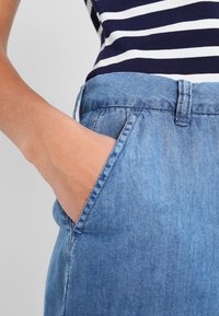 Světle modré džíny se relaxovaným střihem, obsahující přední kapsu a prošitou manžetu. Látka má měkkou a hladkou texturu.