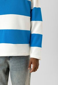 Sweat-shirt en coton rayé bleu et blanc à manches longues, avec un col côtelé et une coupe décontractée, accompagné d'un jean en denim bleu clair.