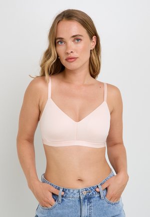 Soutien-gorge rose clair avec un décolleté en V, fabriqué à partir d'un matériau lisse, doté de bretelles ajustables et d'une finition sans coutures. Porté avec un short en denim.