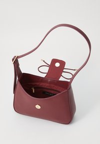 Burgundy leather handbag with a gold button closure, a single shoulder strap, and a spacious interior featuring a zip pocket.