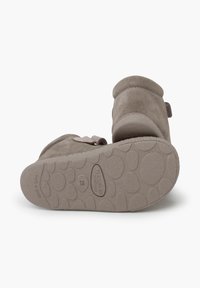 Zapatos slip-on de ante gris con un diseño redondeado. Suela de goma texturizada con patrones circulares y logo en relieve. Sujetados con una correa.