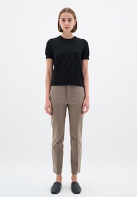 Črn pulover s kratkimi rokavi, kavbojke slim fit v kaki barvi in črnimi čevlji na zavihek. Gladke teksture, minimalističen dizajn, brez vidnih vzorcev ali akcentov.