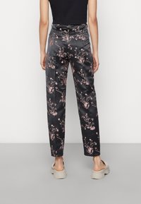 Sorte satinbukser med rosa blomstermønster, lige ben-design og høj talje. Båret med en sort top og beige fodtøj.