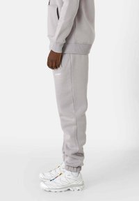 Pantalon de jogging gris en tissu doux, avec poignets côtelés et logo brodé. Associé à des baskets blanches. Vue de côté.