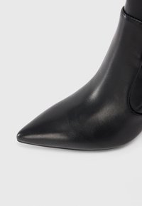 Bottine en cuir noir avec un bout pointu, une texture subtile et une finition lisse. Dotée d'un design épuré avec un minimum de quincaillerie.
