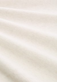 Tissu en coton beige clair avec une texture douce et un léger extensibilité, présentant des plis lisses et fluides avec une variation de couleur minimale.