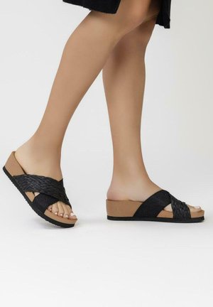 Sandalias deslizantes negras de tejido con base de corcho, que presentan una suela de plataforma y dos correas anchas sobre el pie. Diseño de punta abierta.