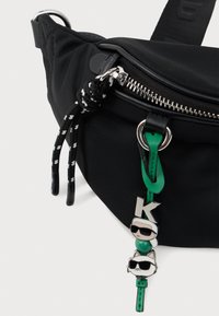 Černá nylonová ledvinka se stříbrným zipem, s zelenými koženými akcenty a jedinečnými charaktery z animovaných filmů připevněnými na poutku zipu.