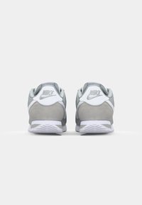 Gray and white Nike sneakers feature a soft suede finish, rounded shape, reinforced heel, and textured rubber outsole for grip.
