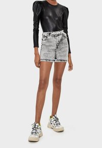 Top negro texturizado de manga larga con hombros abullonados, combinado con una falda mini de mezclilla gris claro. Llevado con zapatillas gruesas blancas que presentan detalles en verde.