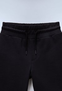 Sorte joggingbukser med snøre i taljen, glat tekstur og detaljer med syninger foran, der viser et enkelt og funktionelt design.