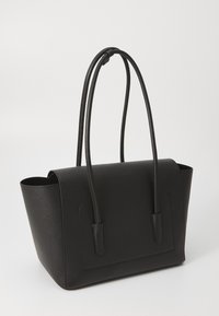 Sac fourre-tout en cuir noir au design structuré, doté de deux longues poignées et d'un rabat supérieur. Surface texturée et accents minimalistes.
