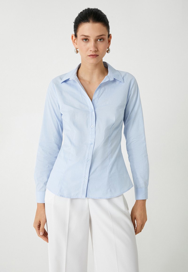 Camisa de botones de manga larga azul claro con collar puntiagudo, diseño ajustado y textura suave. Detalles de botones y puños en color a juego.