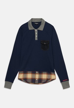 Polo bleu marine à manches longues avec col et poignets gris, poche poitrine noire et détail bas de chemise à carreaux beige.