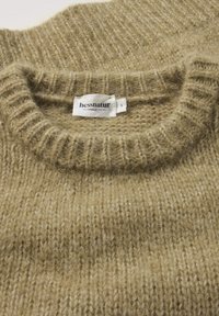 Beige gestrickter Pullover mit ribbeliger Oberfläche und runder Ausschnitt. Etikett sichtbar mit Markenname "hessnatur" und Größe "S".